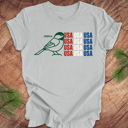 Gray t-shirt with a chickadee bird graphic and 'USA' text on a wooden surface.