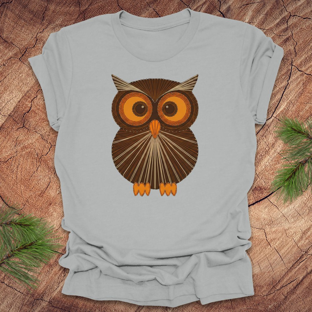 Silver colored t-shirt with a vintage owl design on a wooden surface
