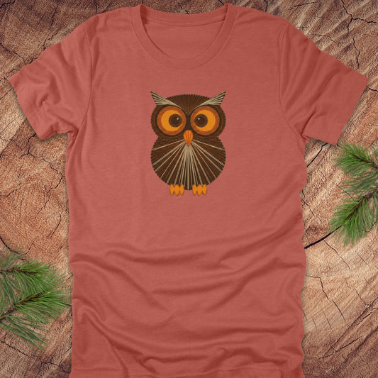 Clay colored t-shirt with a vintage string art owl in browns and oranges on a wood background.