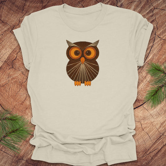 Beige t-shirt with a vintage string art owl in browns and oranges on a wood background.