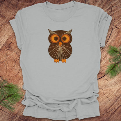 Silver t-shirt with a vintage string art owl in browns and oranges on a wood background.