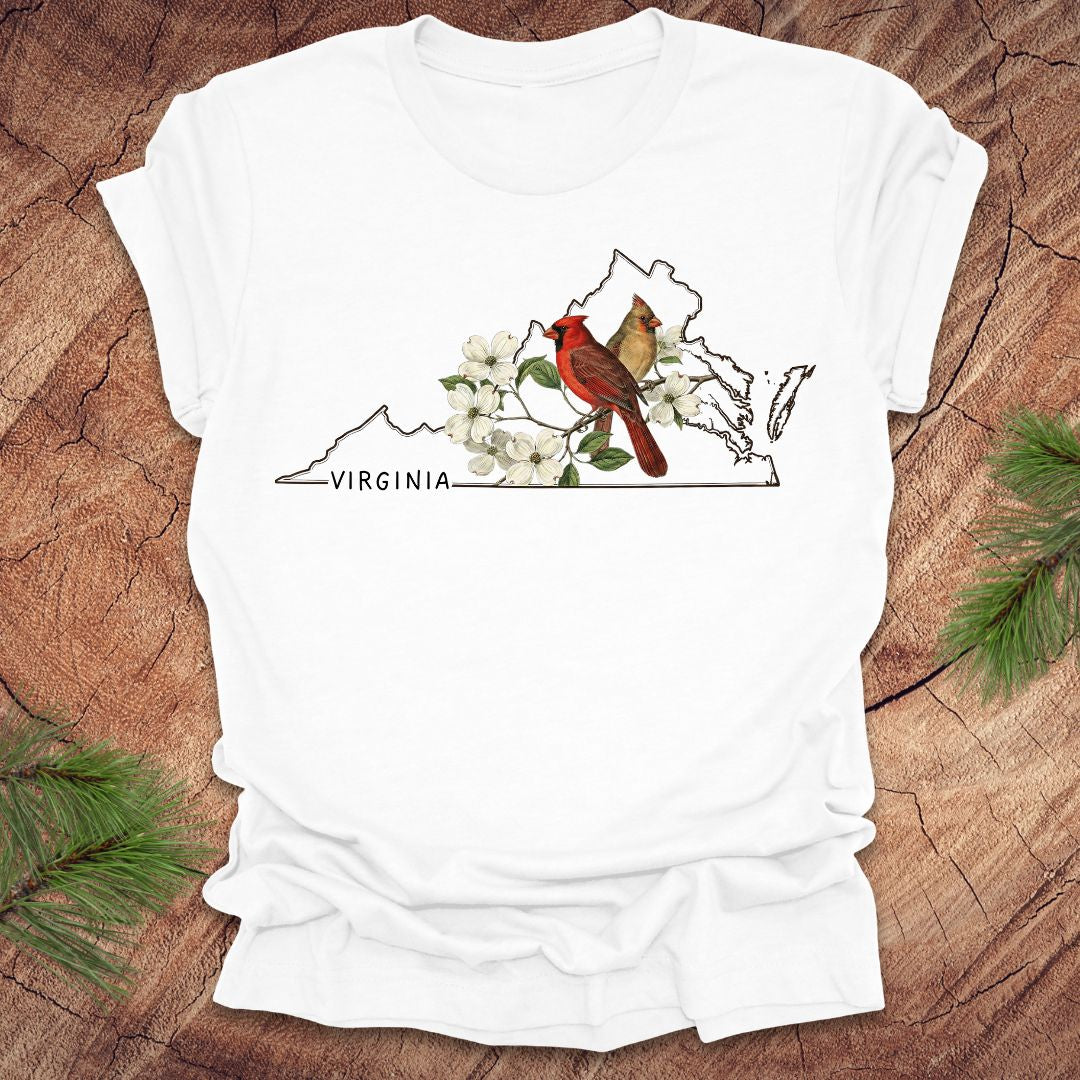 White t-shirt with Virginia map, cardinal, and flowers design on a wooden surface.