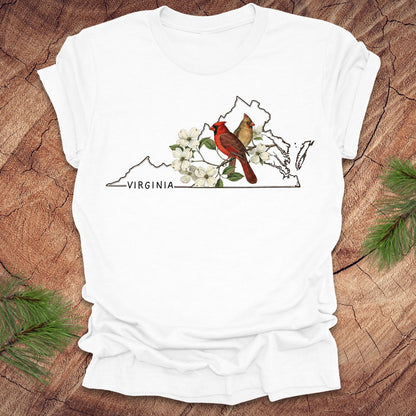 White t-shirt with Virginia map, cardinal, and flowers design on a wooden surface.