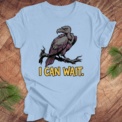 Light blue t-shirt with a vulture graphic and 'I CAN WAIT.' text on a wooden surface.