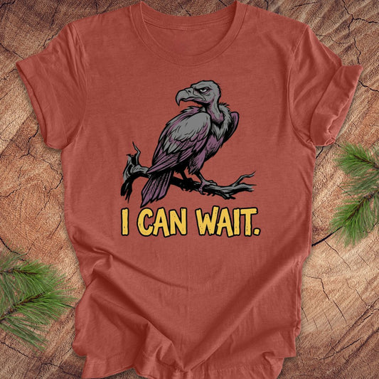 Red t-shirt with a vulture graphic and 'I CAN WAIT.' text on a wooden surface.