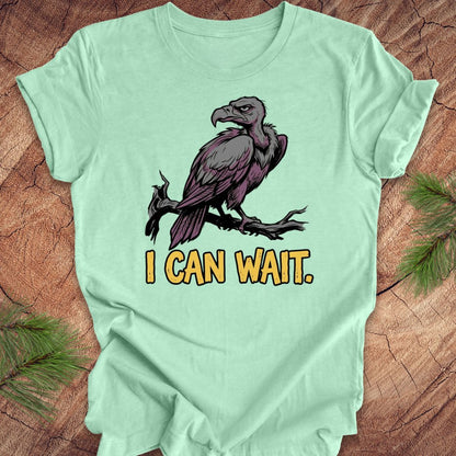 Light green t-shirt with a vulture graphic and 'I CAN WAIT.' text on a wooden surface.