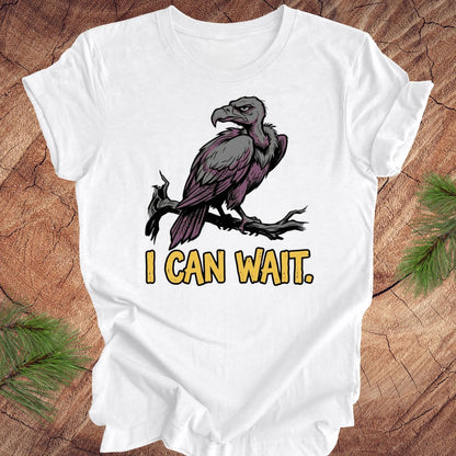 White t-shirt with a vulture graphic and 'I CAN WAIT.' text on a wooden surface.