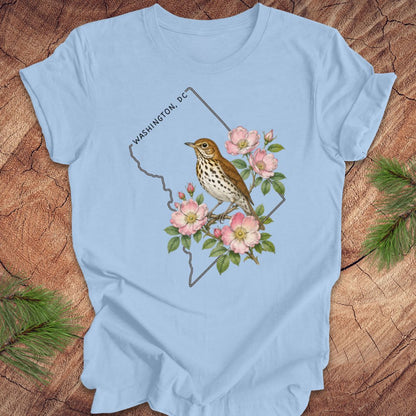 Blue t-shirt with a Washington DC outline and  thrush and rose design on a wooden surface