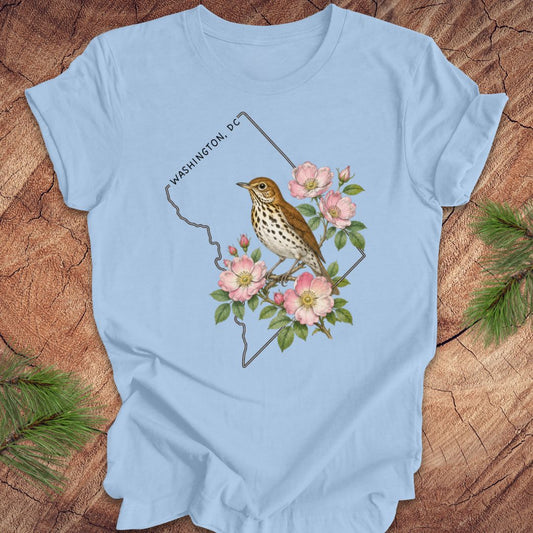 Blue t-shirt with a Washington DC outline and  thrush and rose design on a wooden surface