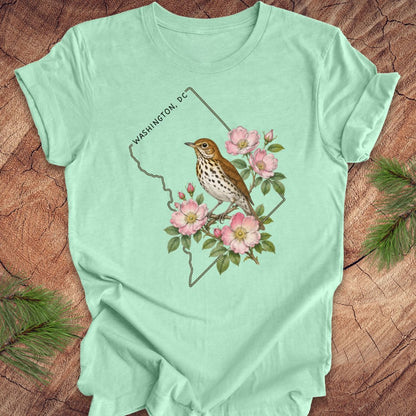 Mint green t-shirt with a Washington DC outline and  thrush and rose design on a wooden surface