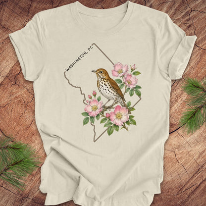 Beige t-shirt with a Washington DC outline and  thrush and rose design on a wooden surface