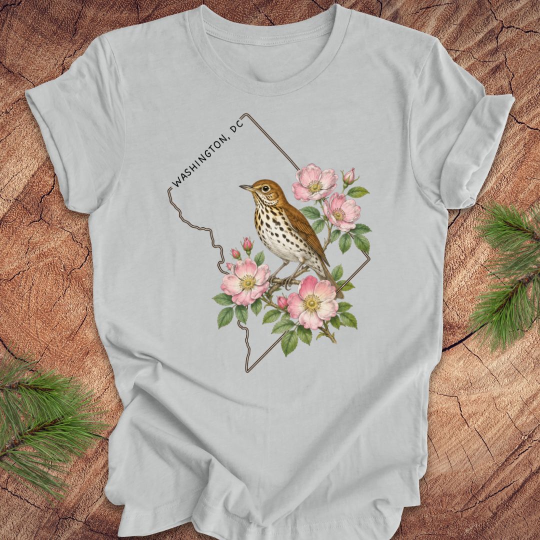 Gray t-shirt with a Washington DC outline and  thrush and rose design on a wooden surface