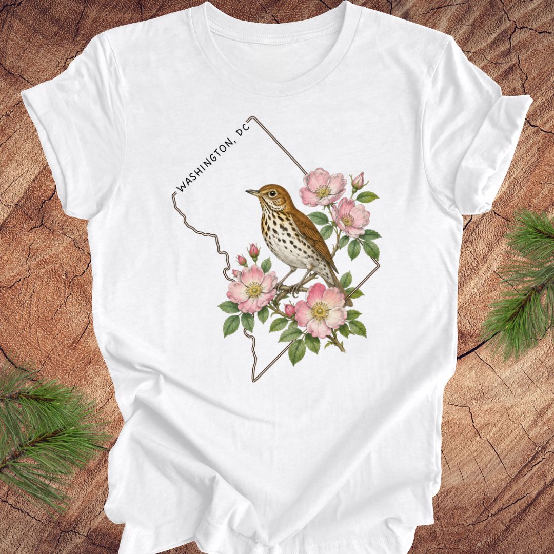 White t-shirt with a Washington DC outline and  thrush and rose design on a wooden surface
