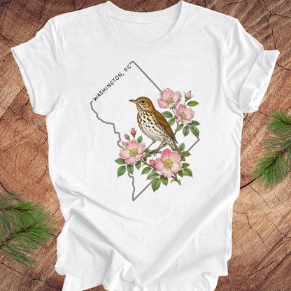 White t-shirt with a Washington DC outline and  thrush and rose design on a wooden surface