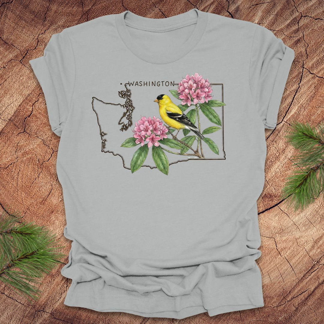 Silver t-shirt with Washington state outline with state bird goldfinch and rhododendron on a wood background.