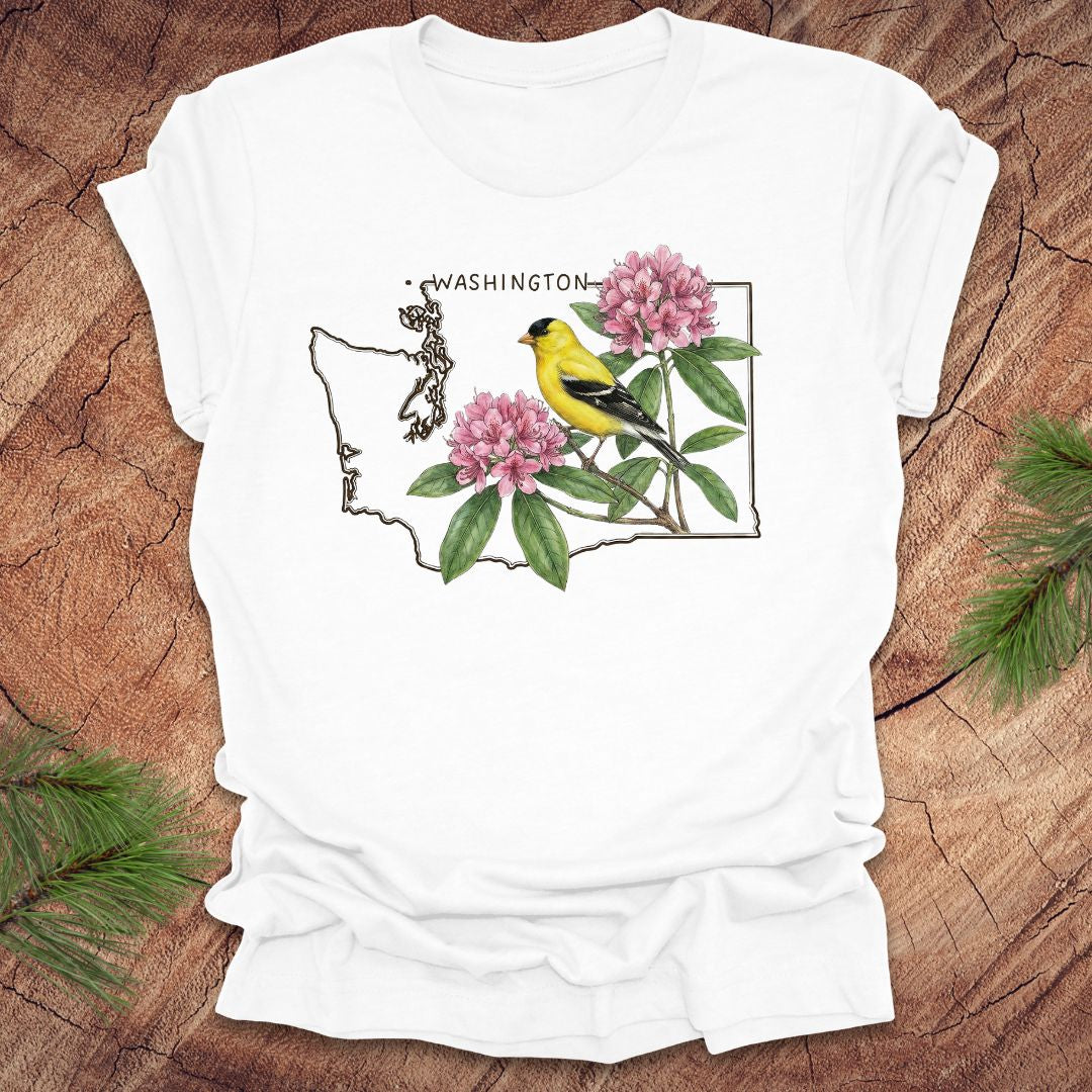 White t-shirt with Washington state outline with state bird goldfinch and rhododendron on a wood background.