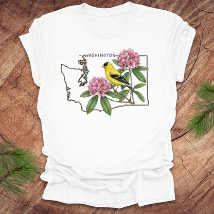 White t-shirt with Washington state outline with state bird goldfinch and rhododendron on a wood background.