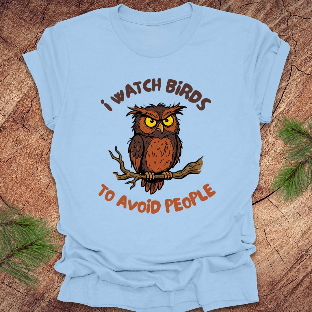 Light blue t-shirt with an owl graphic and text, 'I watch birds to avoid people' on a wooden background