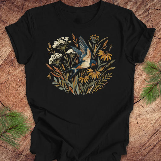 Black t-shirt with watercolor flowers and a barn swallow in flight, on a wood background. 