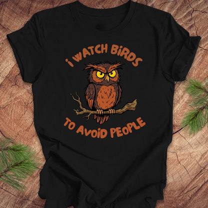 Black t-shirt with an owl graphic and text, 'I watch birds to avoid people' on a wooden background
