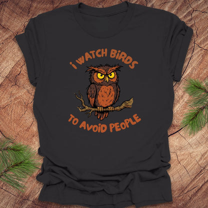 Dark gray t-shirt with an owl graphic and text, 'I watch birds to avoid people' on a wooden background