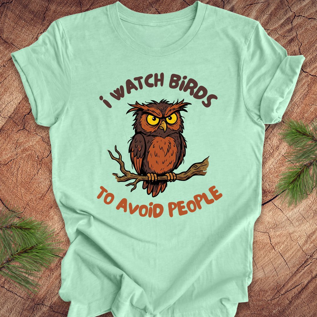 Heather mint t-shirt with an owl graphic and text, 'I watch birds to avoid people' on a wooden background