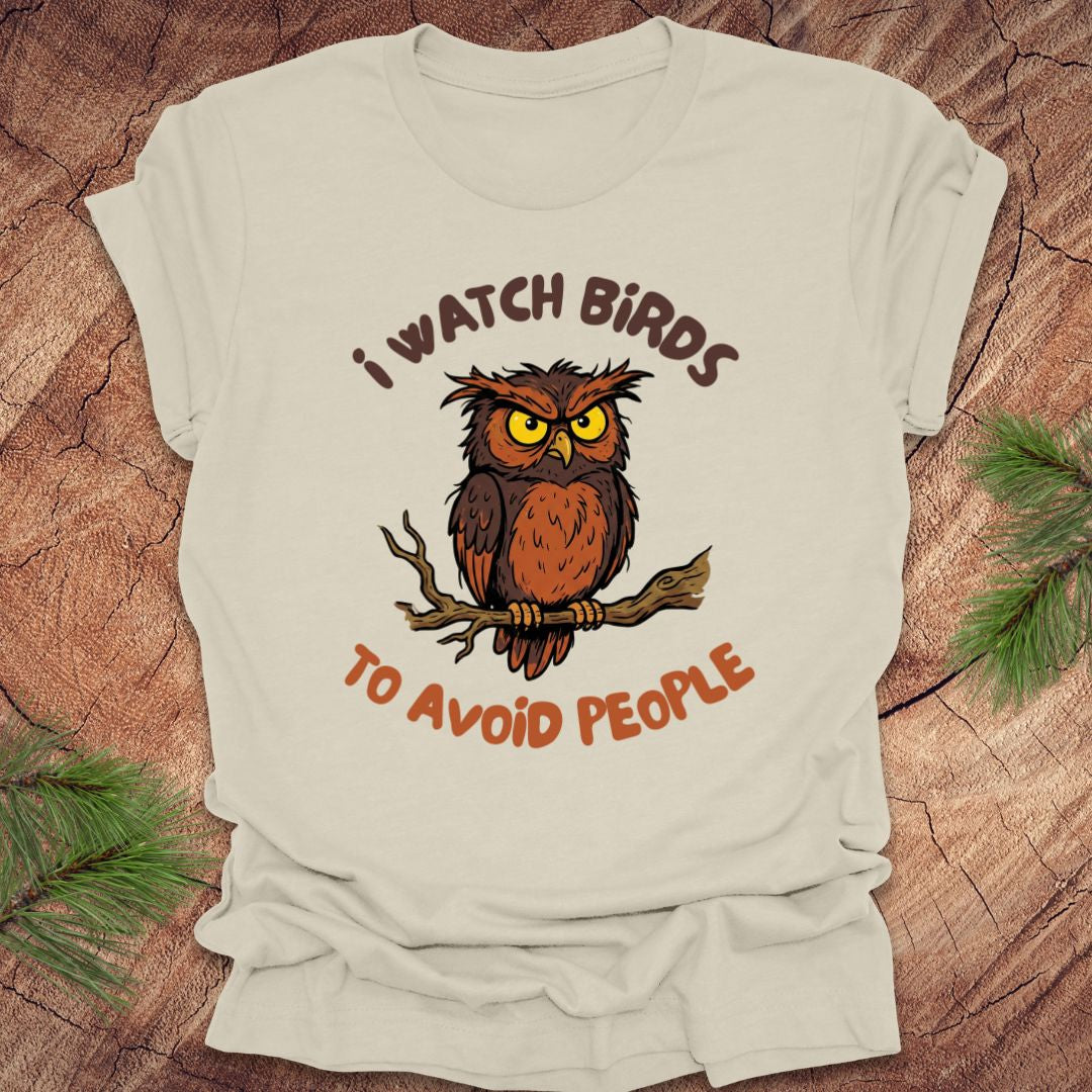 Beige t-shirt with an owl graphic and text, 'I watch birds to avoid people' on a wooden background