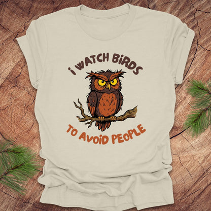 Beige t-shirt with an owl graphic and text, 'I watch birds to avoid people' on a wooden background