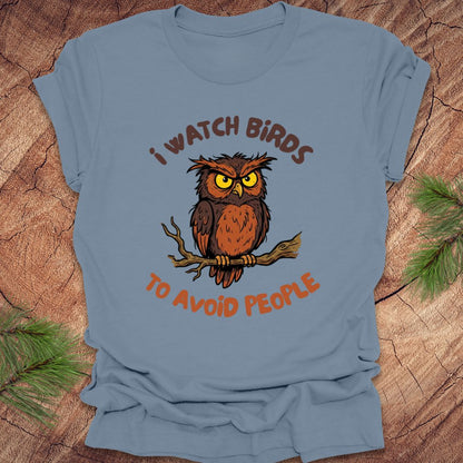 Steel blue t-shirt with an owl graphic and text, 'I watch birds to avoid people' on a wooden background