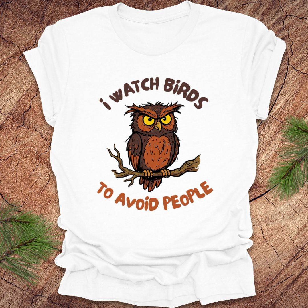 White t-shirt with an owl graphic and text, 'I watch birds to avoid people' on a wooden background