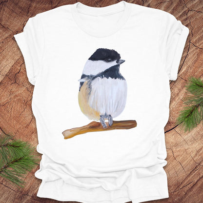 White t-shirt with a watercolor chickadee on a wooden surface