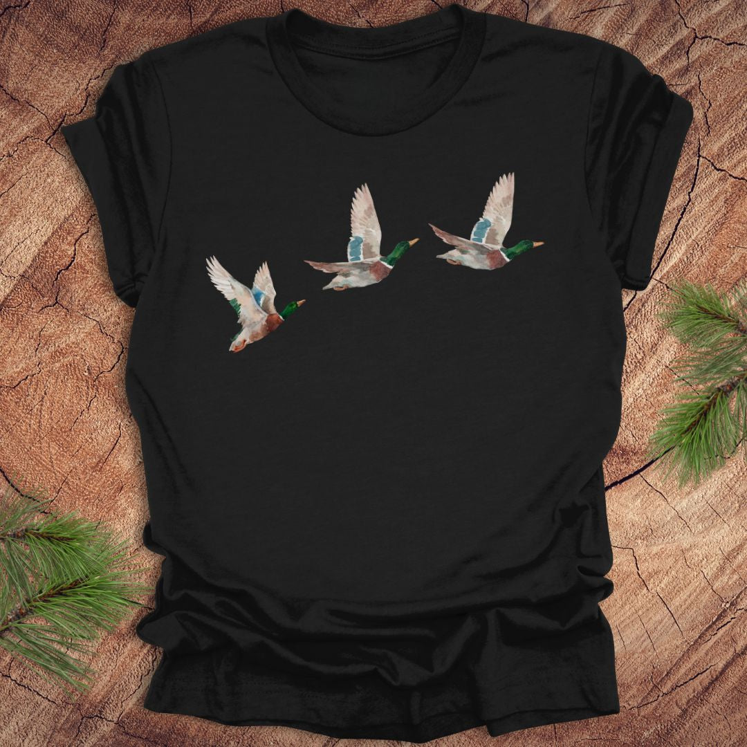 Black t-shirt with three flying watercolor mallard duck designs on a wooden surface.