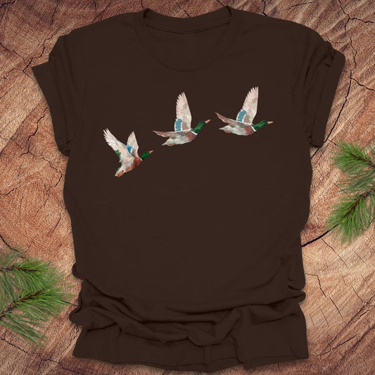 Brown t-shirt with three flying watercolor mallard duck designs on a wooden surface.