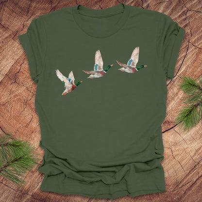 Mililtary green t-shirt with three flying watercolor mallard duck designs on a wooden surface.