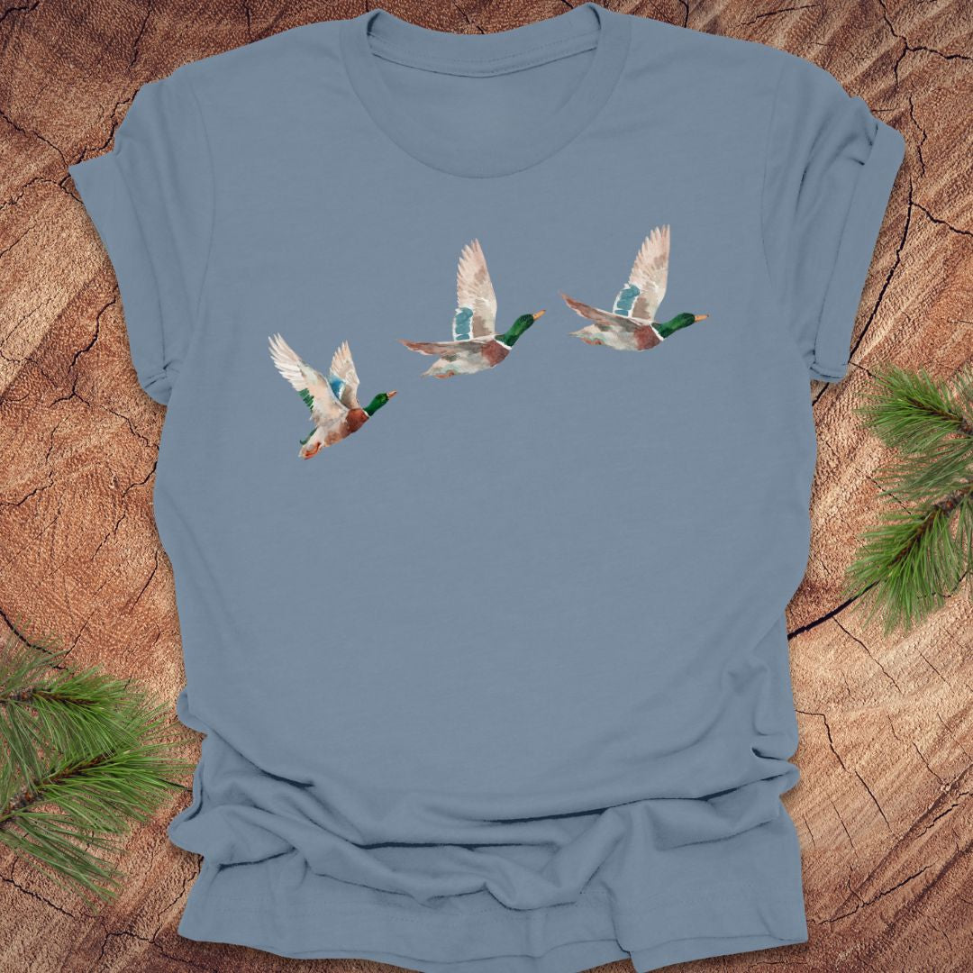 Steel blue t-shirt with three flying watercolor mallard duck designs on a wooden surface.