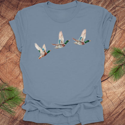 Steel blue t-shirt with three flying watercolor mallard duck designs on a wooden surface.