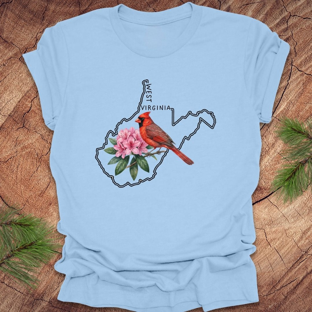 Baby blue t-shirt with the outline of West Virginia and its state bird,and flower cardinal and  rhododendron, on a wooden background.