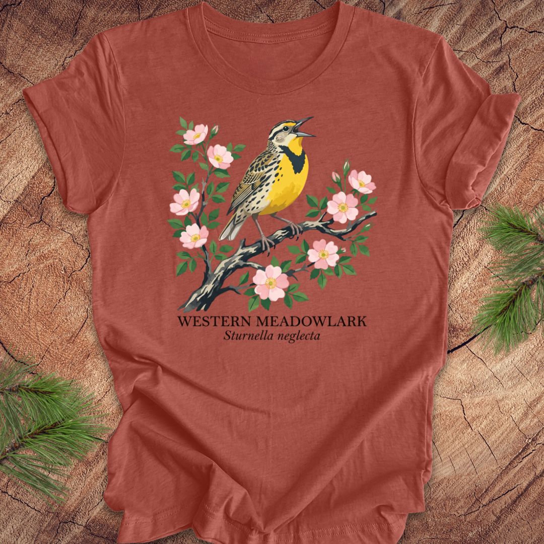 Clay colored t-shirt with a Western Meadowlark graphic on a wooden surface