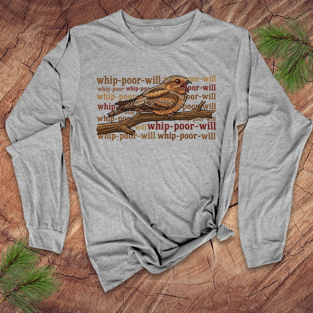 Gray long-sleeve shirt with a bird graphic and repeated 'whip-poor-will' text on a wooden surface.