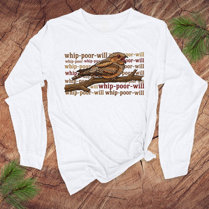 White long-sleeve shirt with a bird graphic and repeated 'whip-poor-will' text on a wooden surface.