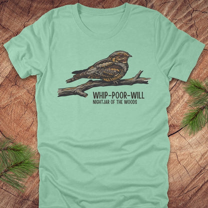 Mint green t-shirt with a whip-poor-will bird on a branch with text 'nightjar of the woods' on a wood background.