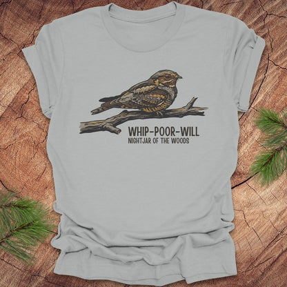 Silver t-shirt with a whip-poor-will bird on a branch with text 'nightjar of the woods' on a wood background.