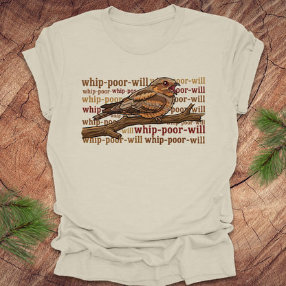 Beige t-shirt with a bird graphic and 'whip-poor-will' text on a wooden surface.
