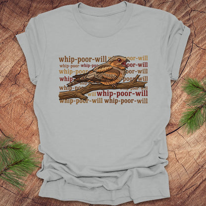 Light gray t-shirt with a bird graphic and 'whip-poor-will' text on a wooden surface.