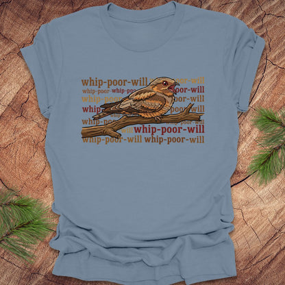 Blue t-shirt with a bird graphic and 'whip-poor-will' text on a wooden surface.
