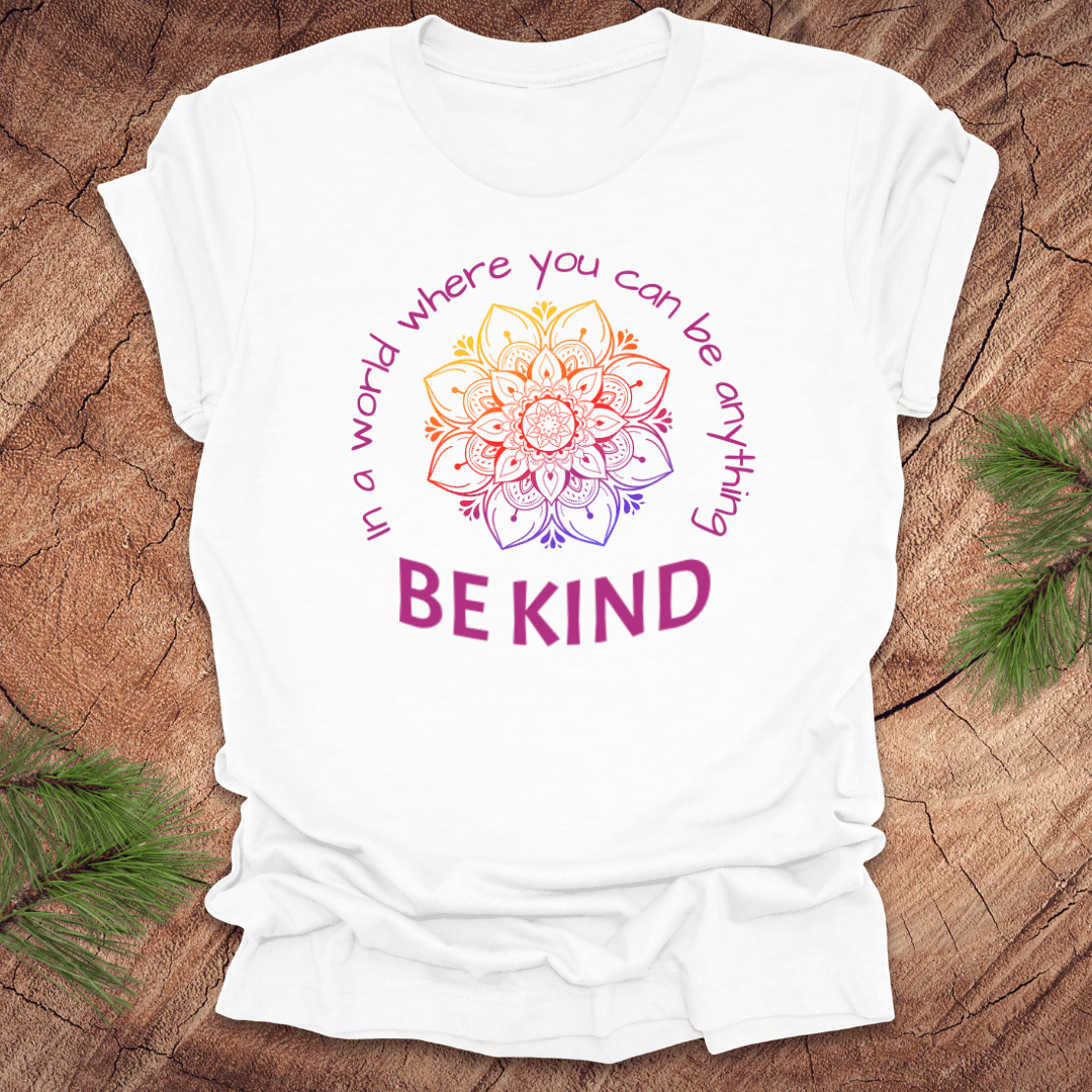 White t-shirt with a colorful mandala and 'Be Kind' text on a wooden surface.