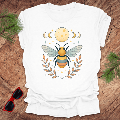 White tshirt with a bee and moon graphic on a wood background.