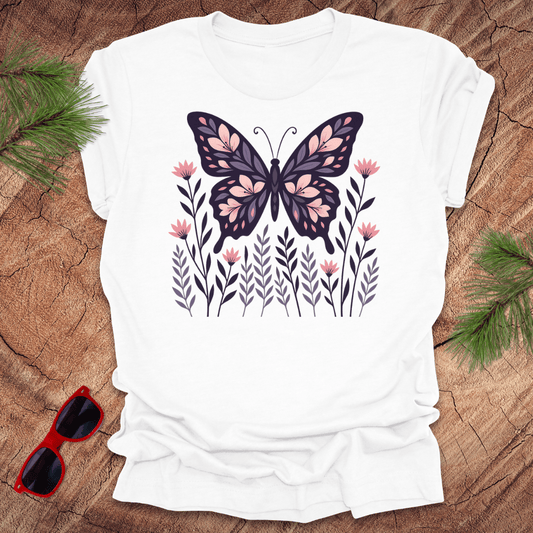 White t-shirt with a butterfly and flower design on a wooden surface with sunglasses and leaves.