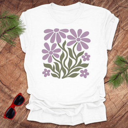 White t-shirt with purple floral design on a wooden surface with sunglasses and greenery.