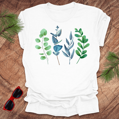 White t-shirt with leaf designs on a wooden surface with sunglasses and greenery.